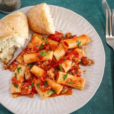 Overhead shot of a plate of rigatoni with a bright and flavorful sausage ragu made with Italian sausage, hand-crushed tomatoes, garlic, and onions.