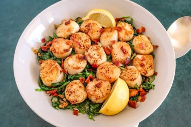 Serving dish of scallops on spinach with bacon.