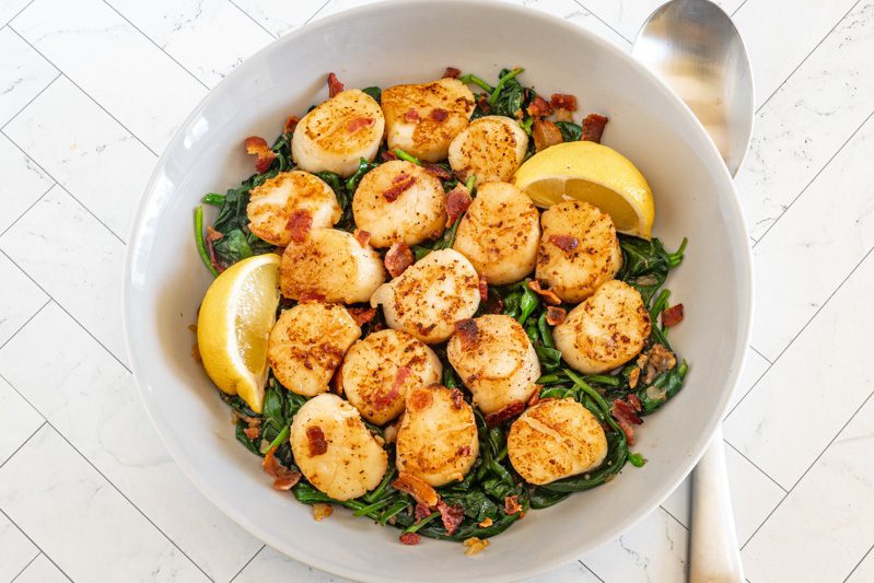 seared scallops in a serving dish on spinach with bacon