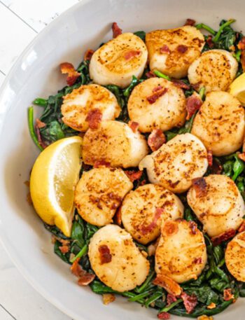 scallops on a bed of spinach with lemon wedges and bits of bacon