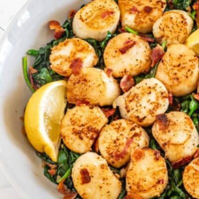 scallops on a bed of spinach with lemon wedges and bits of bacon