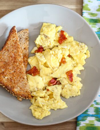 a plate of scrambled eggs with bacon and slices of toast on the side