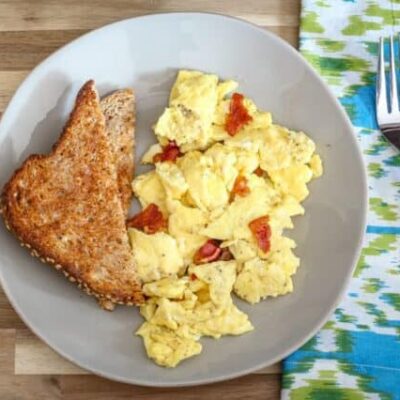 a plate of scrambled eggs with bacon and slices of toast on the side