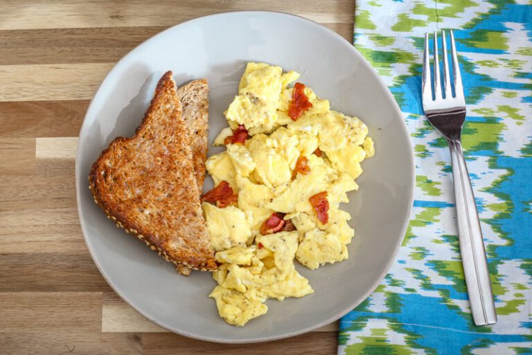 a plate of scrambled eggs with bacon and slices of toast on the side