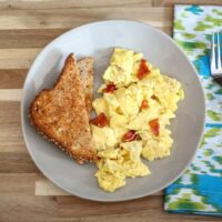 scrambled eggs with bacon on a plate with sliced toast