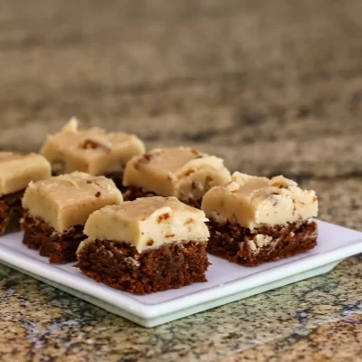 Fudge brownie bars topped with creamy white chocolate and nuts on a small square plate.