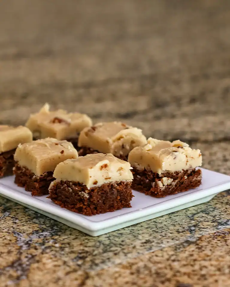 Fudge brownie bars topped with creamy white chocolate and nuts on a small square plate.