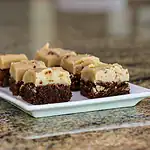 Fudge layered dessert with a chocolate crust and creamy topping on a white plate.