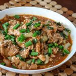 sesame pork in a serving bowl with green onions