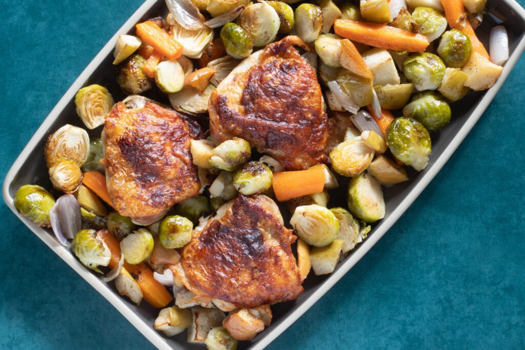 roasted chicken thighs and vegetables, including brussels sprouts, carrots, apples, and shallots
