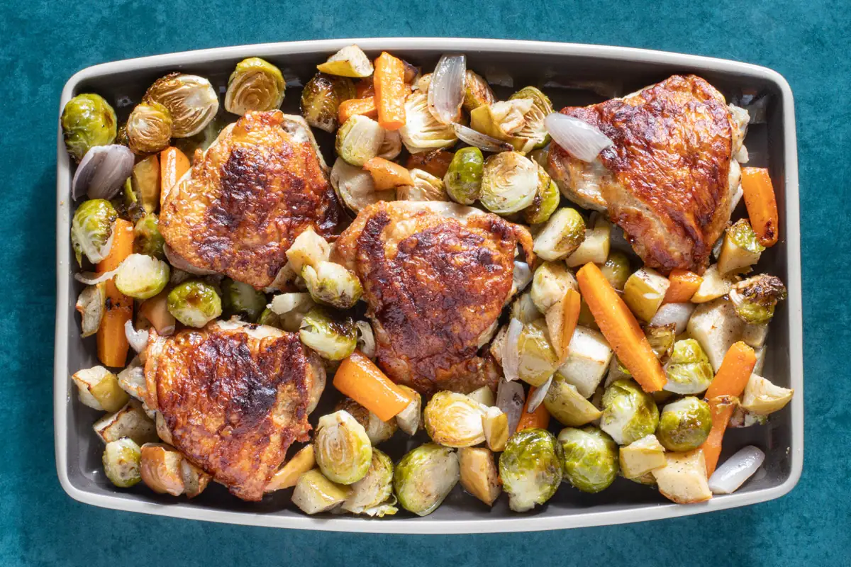 A tray of sheet pan chicken thighs with brussels sprouts and other fall vegetables.