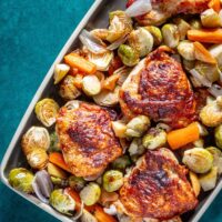 A serving tray with crispy chicken thighs, apples, and fall vegetables.