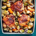 A serving tray with crispy chicken thighs, apples, and fall vegetables.