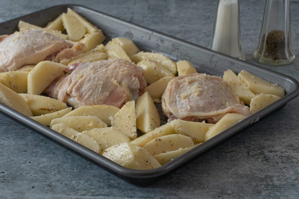 arranging the chicken thighs and potatoes on the baking sheet.