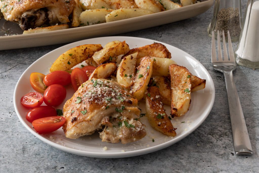 sheet pan chicken thighs and potatoes with parmesan cheese and garlic, on a plate