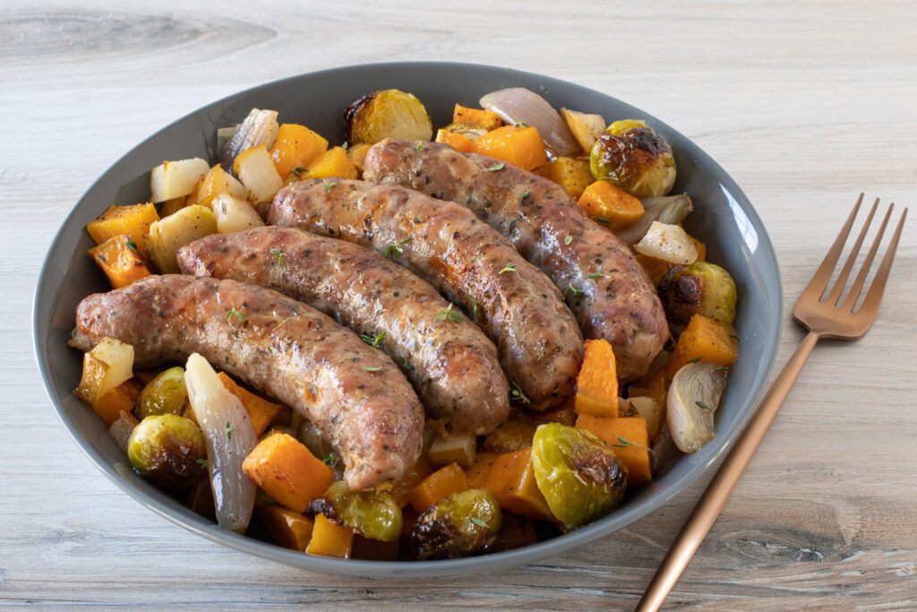 A serving dish with sausages, butternut squash, brussels sprouts, and diced pears.