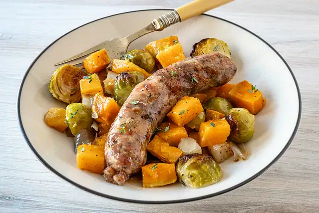 A serving of sheet pan sausage with sweet potatoes, Brussels sprouts, butternut squash, and pears.