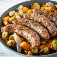 Grilled sausages served with roasted vegetables on a dark plate.