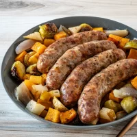 Grilled sausages with roasted vegetables on a dark plate.