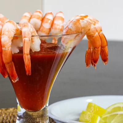 Succulent shrimp hanging on the rim of a cocktail glass filled with a red drink.