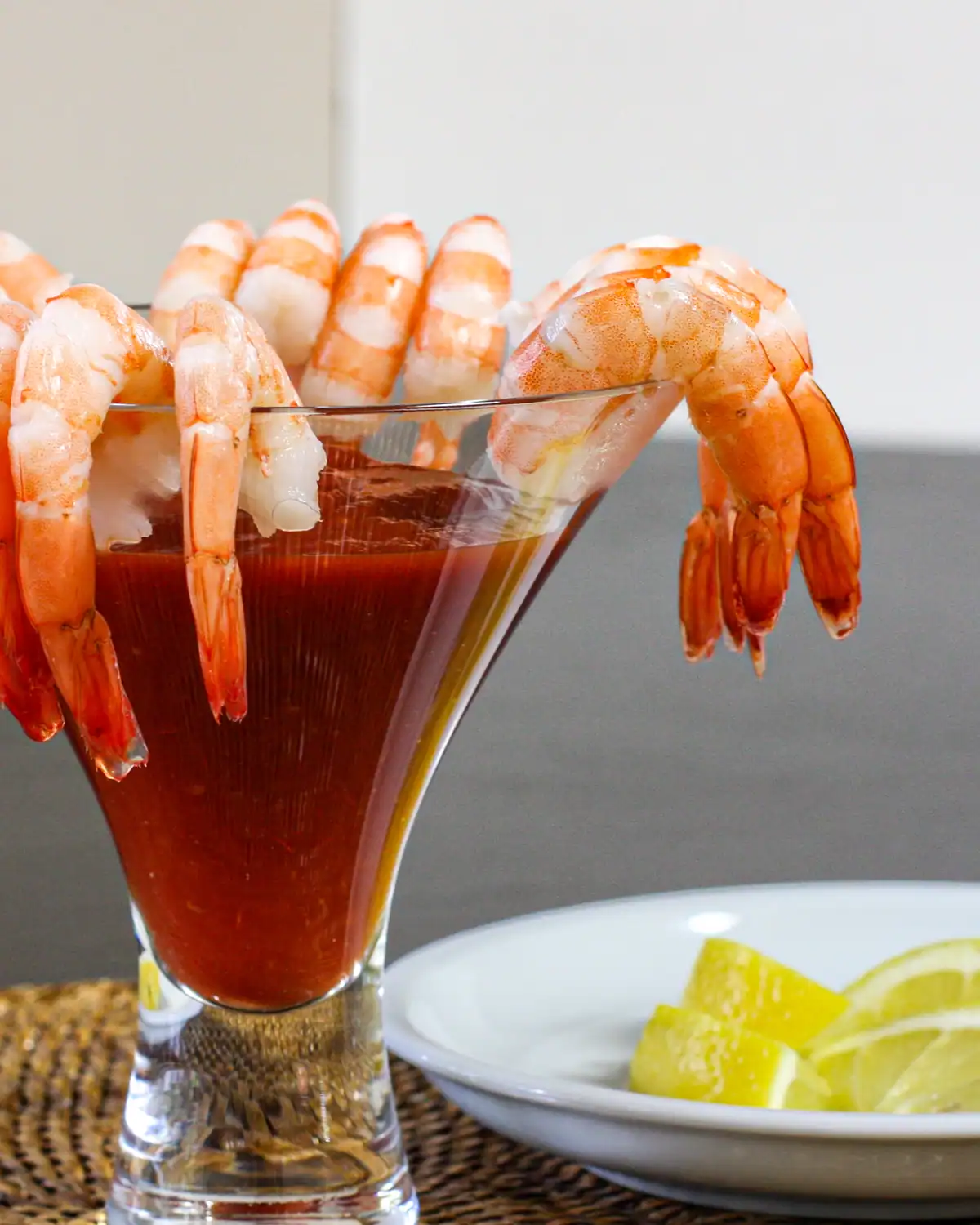 Succulent shrimp hanging on the rim of a cocktail glass filled with a red drink.