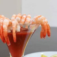 Shrimp and cocktail sauce in a modern martini glass with lemon wedges on the side.