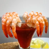 Fresh shrimp hanging on the rim of a cocktail glass filled with red sauce.