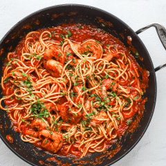Savory spaghetti with shrimp in tomato sauce garnished with chopped herbs.