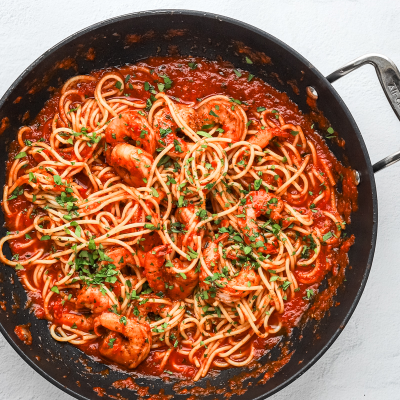 Savory spaghetti with shrimp in tomato sauce garnished with chopped herbs.