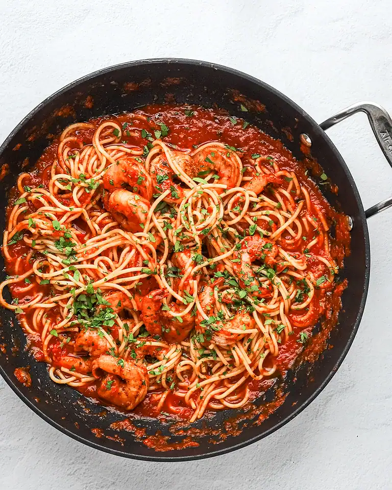 Savory spaghetti with shrimp in tomato sauce garnished with chopped herbs.