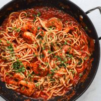 Spaghetti with shrimp in tomato sauce topped with chopped parsley.