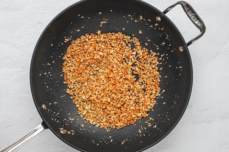 Golden toasted bread crumbs in a black frying pan on a light gray surface.