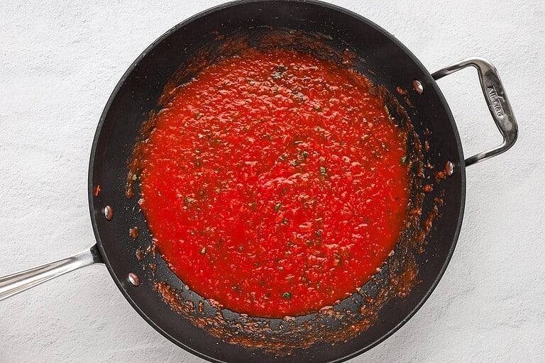 Rich tomato sauce simmering in a black skillet.