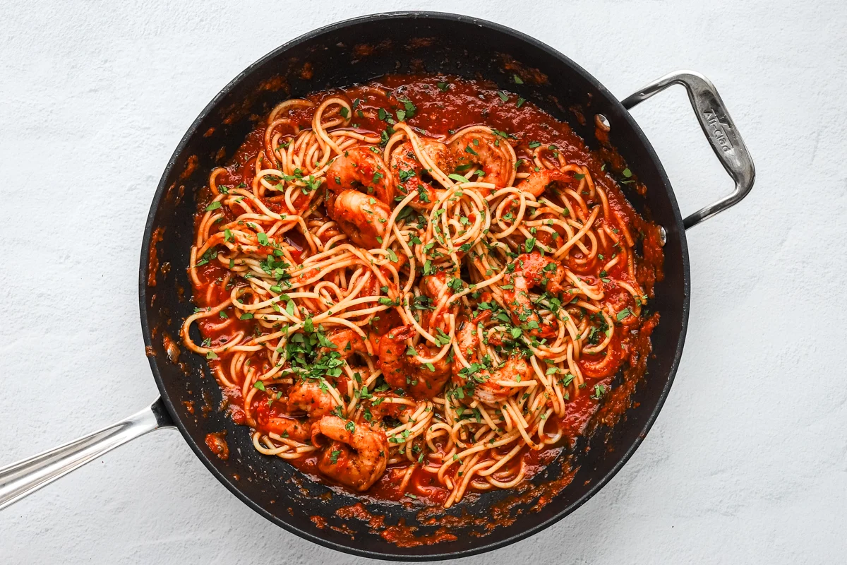 Preparing shrimp fra diavolo in the skillet with spaghett, red tomato sauce, shrimp, and parsley.