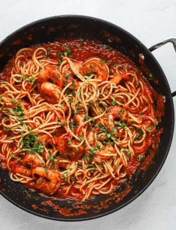Preparing shrimp fra diavolo in the skillet with spaghetti, red tomato sauce, shrimp, and parsley.