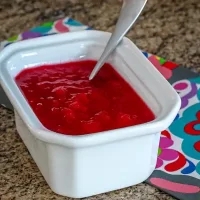 Fresh strawberry jam in a white ceramic dish with a spoon.