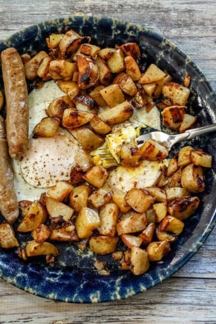 Home fries on a plate with eggs and sausages.