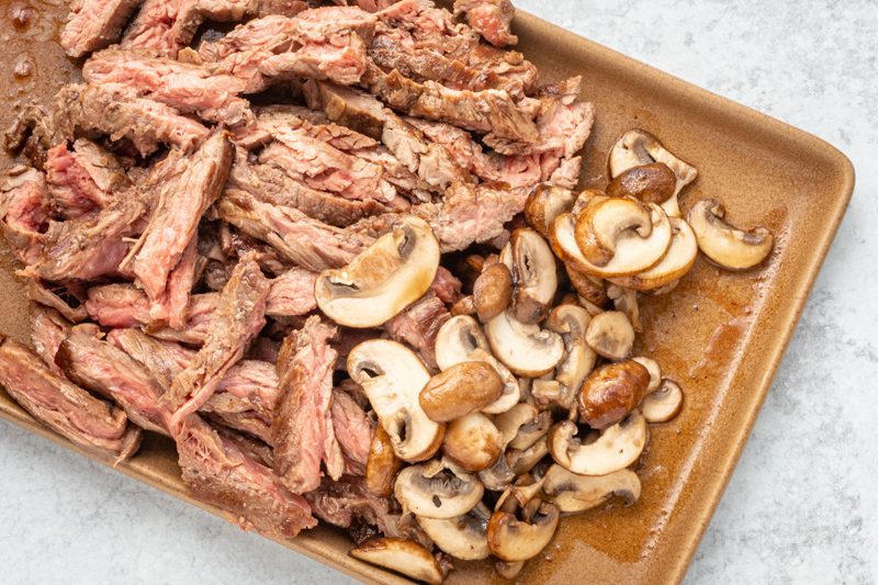 Sliced skirt steak and mushrooms on a platter for a philly cheesesteak skillet recipe