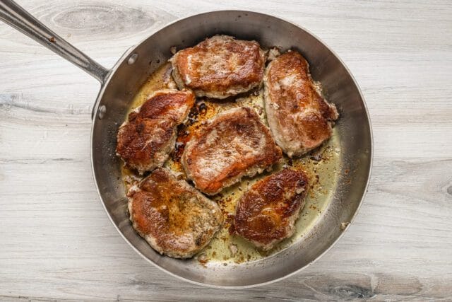 Golden-brown seared pork chops in a frying pan.