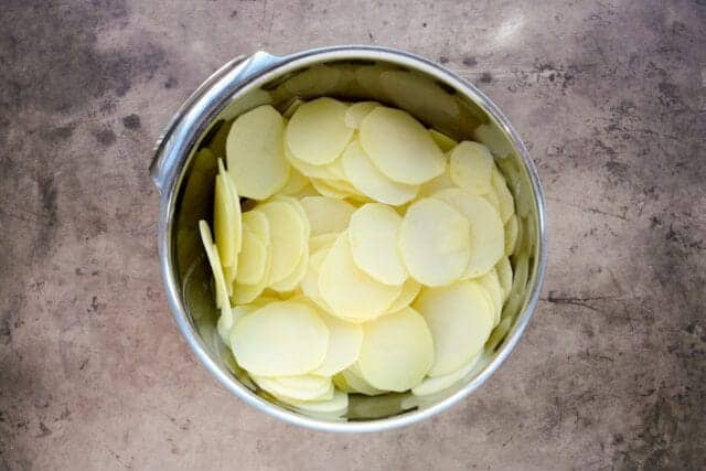 Thinly sliced potatoes in a stainless steel bowl.