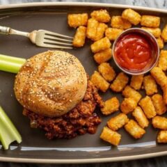 sloppy joe sandwich with tater tots and ketchup on the side.