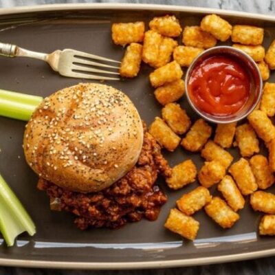 sloppy joe sandwich with tater tots and ketchup on the side.