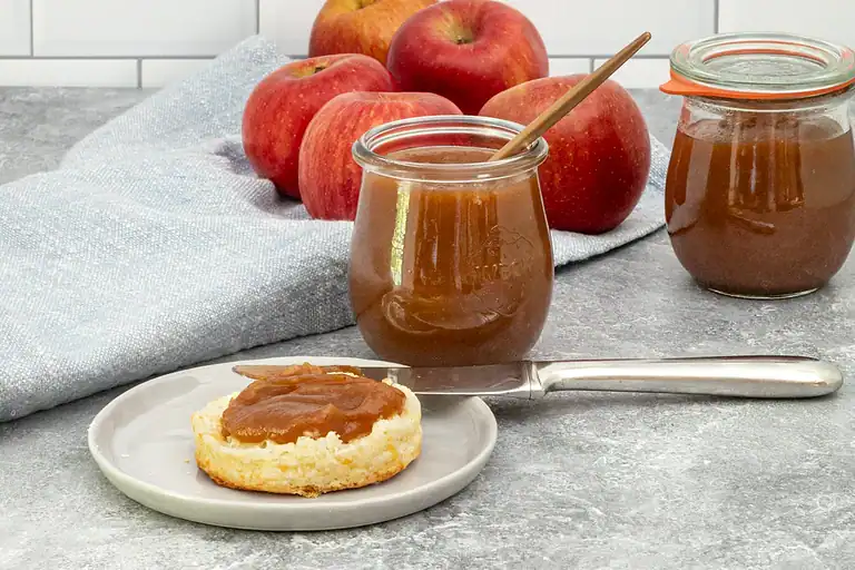 Homemade applesauce jar with a spoon on a kitchen counter.