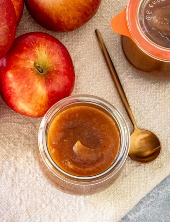 Overhead photo of slow cooker apple butter in a canning jar with apples on the side.