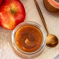 Creamy apple butter in a glass jar with fresh apples nearby.