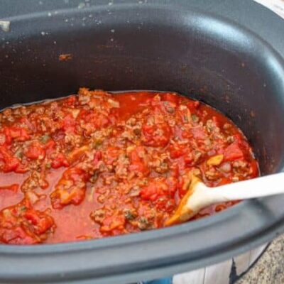 slow cooker bolognese sauce in the slow cooker with a wooden spoon