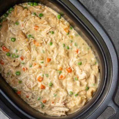 The slow cooker with finished chicken and dumplings made with refrigerated biscuits and peas and carrots.