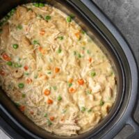 The slow cooker with finished chicken and dumplings made with refrigerated biscuits and peas and carrots.