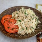 slow cooker parisienne shown on a plate with angel hair pasta and sliced tomatoes