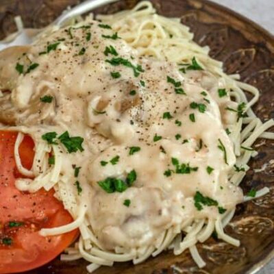 slow cooker chicken parisienne over pasta with sliced tomatoes on the side